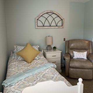 A cozy bedroom with a single bed, recliner chair, and a decorative wall piece.
