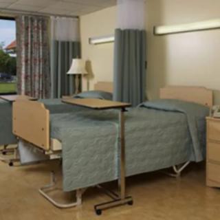 A hospital room with two beds separated by curtains and equipped with medical furniture.