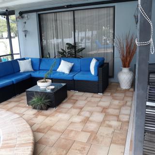 A cozy outdoor patio with a blue cushioned sofa and a small coffee table surrounded by decorative plants.