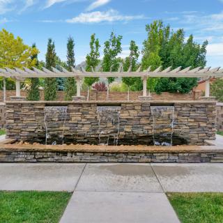 A stone fountain with cascading water surrounded by a lush garden and pathway.