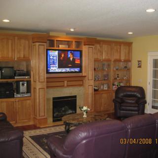 A cozy living room featuring leather seating, a television mounted above a fireplace, and wooden cabinetry.
