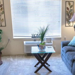 A cozy living room with a comfortable sofa, side table with decor, and a window with blinds letting in natural light.