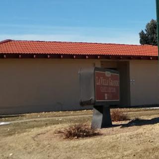 A view of a building with a red tiled roof and a sign in front, set against a clear blue sky.