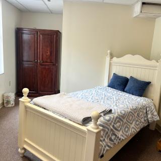 A cozy bedroom featuring a white bed with decorative pillows and a wooden wardrobe.