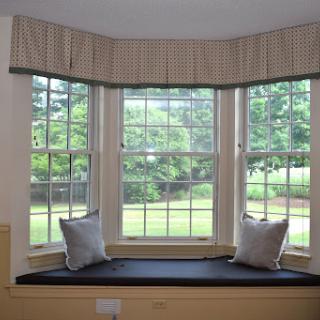 A cozy bay window with a seating area, adorned with soft pillows and curtains, inviting natural light into the room.