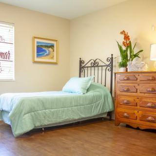A cozy bedroom with a single bed, wooden dresser, and bright natural light.