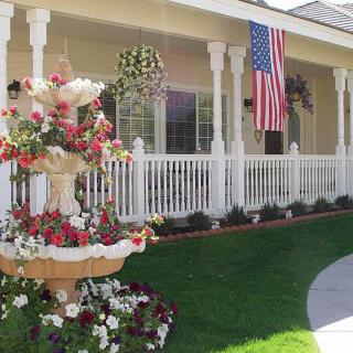 A charming house with a white porch, beautifully landscaped garden, and an American flag displayed prominently.