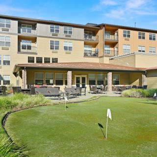 A modern apartment building with a small putting green in the foreground, surrounded by landscaped greenery.