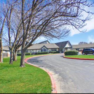 A picturesque view of a building surrounded by trees and well-maintained grass, with a winding road leading up to it.