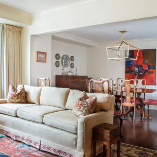 A cozy living room with a beige sofa and an adjoining dining area featuring stylish artwork.