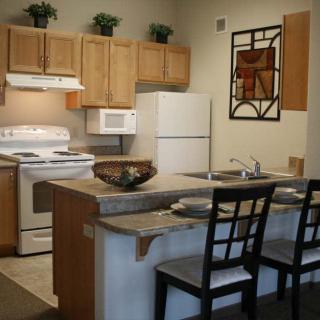 A modern kitchen interior featuring wooden cabinets, a white refrigerator, and bar seating.