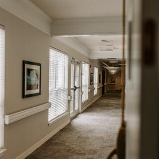 A quiet, well-lit hallway with artwork and windows along one side.