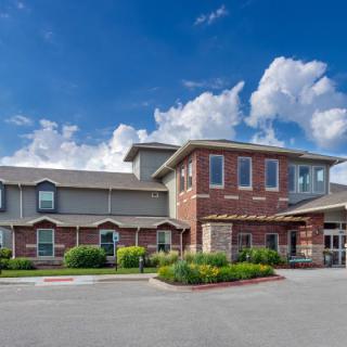 A two-story brick building under a partly cloudy sky, surrounded by landscaped greenery.