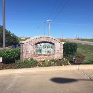 A brick sign surrounded by landscaped bushes and flowers under a clear blue sky.