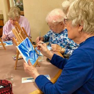 A group of seniors engaged in a painting class, each working on their own artistic creation.