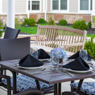 An elegantly set outdoor dining table with black napkins and patio furniture, situated in a garden setting.