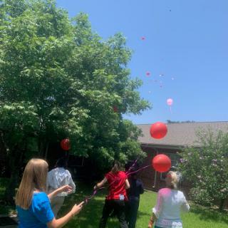 A group of people enjoying a sunny day outdoors, releasing red balloons into the sky.