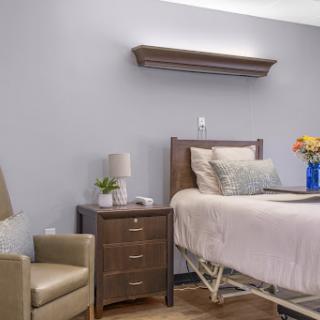 A well-organized patient room featuring a bed, nightstand with a lamp, and a comfortable chair.