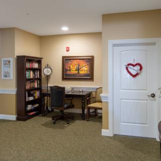 A cozy office space with a bookshelf, desk, and chair, adorned with a painting and wall decor.