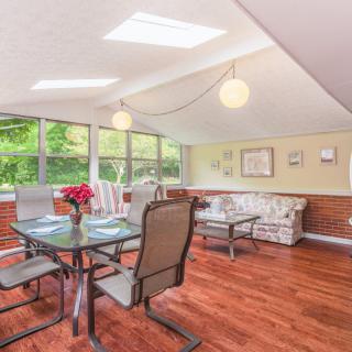 A modern dining room with large windows and skylights, featuring a glass-top table and comfortable seating.