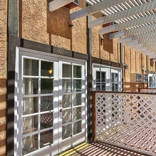 A sunny outdoor space featuring a pergola with intricate shadows cast on the building facade and glass doors.