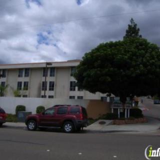 A street view of a residential building with parked cars under a cloudy sky.