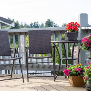 A cozy patio setup with chairs, a table, and vibrant flowers on a deck.