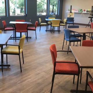 An empty cafeteria with colorful chairs and wooden flooring.