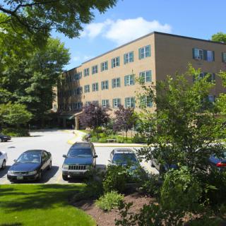 A sunny view of an office building with a parking lot surrounded by trees and well-maintained landscaping.