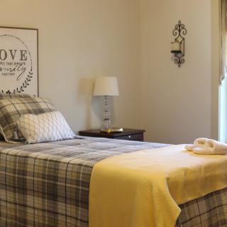A cozy bedroom with plaid bedding and a yellow blanket, featuring a lamp on the nightstand and wall art for decoration.