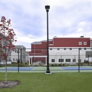 A tennis court enclosed by a fence with a lamp post nearby, adjacent to a building.