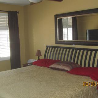 A cozy bedroom with a large bed, accented by red pillows, and a mirror above the headboard.