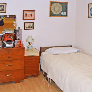 A vintage-style bedroom with a single bed and wooden dresser adorned with decorative items and wall art.