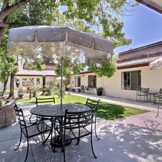 A sunny patio with an iron table and chairs under a large umbrella, surrounded by trees and garden space.