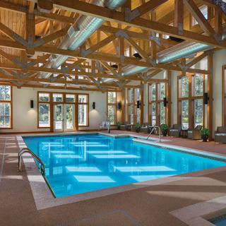An elegant indoor swimming pool with wooden beam architecture and large windows.