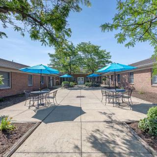 A sunny courtyard with tables, chairs, and umbrellas surrounded by brick buildings.