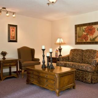 A cozy living room featuring a sofa, chairs, wooden coffee table with candles, and decorative art on the walls.