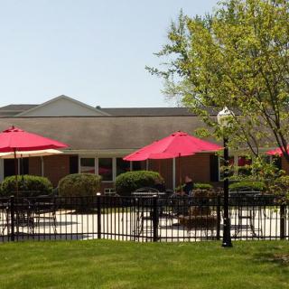 A sunny patio area with red umbrellas and seating, surrounded by a black fence and greenery.