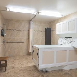 A modern, accessible bathroom with a tiled floor and a bathtub equipped with handrails.