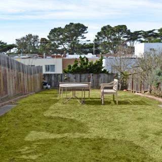 A backyard with a grass lawn and outdoor furniture surrounded by a wooden fence.