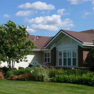 A suburban house with a well-maintained front yard and garden under a blue sky with scattered clouds.