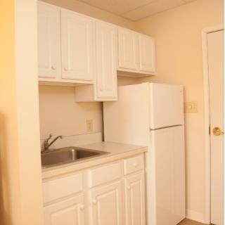 A compact apartment kitchen with white cabinets and a refrigerator.