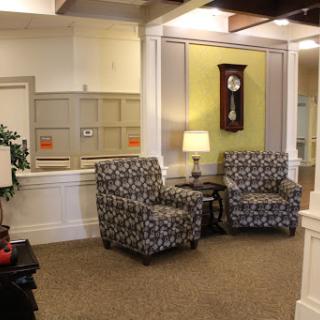 A cozy seating area featuring patterned chairs, a lamp, and a wall clock.