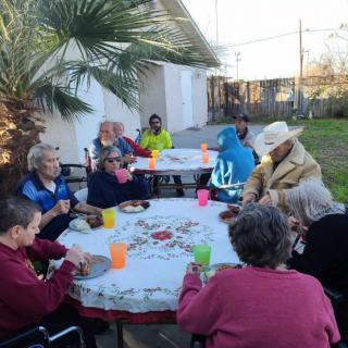A group of people enjoying an outdoor gathering around a table in a garden setting.