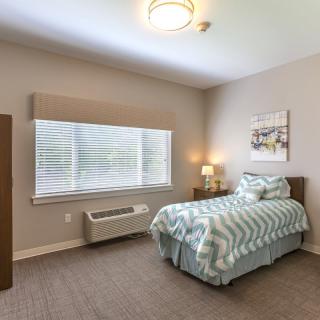 A minimalist bedroom with a single bed, bedside lamp, and a large window covered by curtains.