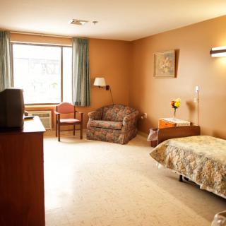 A cozy room with a bed, chair, and television by the window.