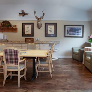 A cozy dining area with wooden flooring, featuring a table and chairs, decorative art on the walls, and a deer head mount.
