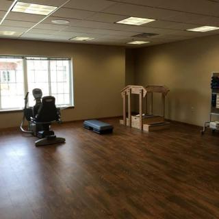An empty fitness room with exercise equipment and wooden flooring.