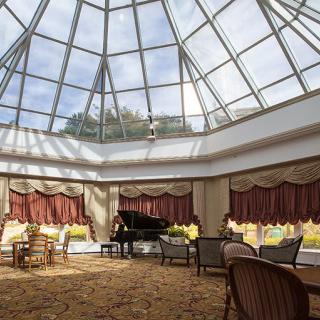 A spacious lounge area with a grand piano under a glass atrium, featuring elegant furniture and ample natural light.