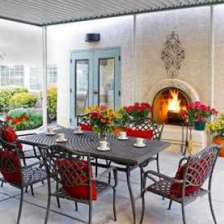 A cozy patio with a fireplace and a dining area surrounded by colorful flowers.